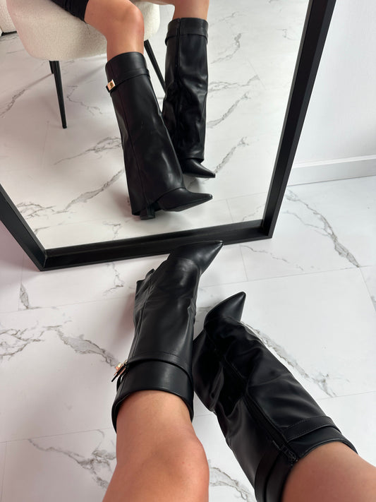 Black knee-high boots being worn on a marble floor with a mirror reflection.