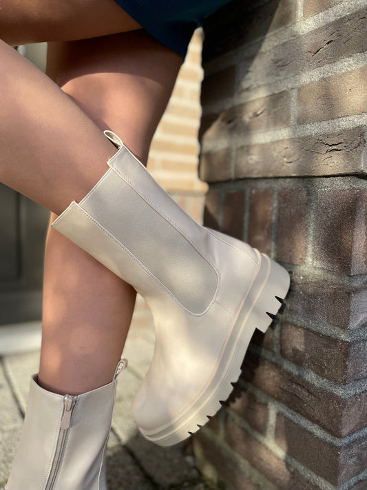 White transparent rain boots worn by a person sitting against a brick wall.